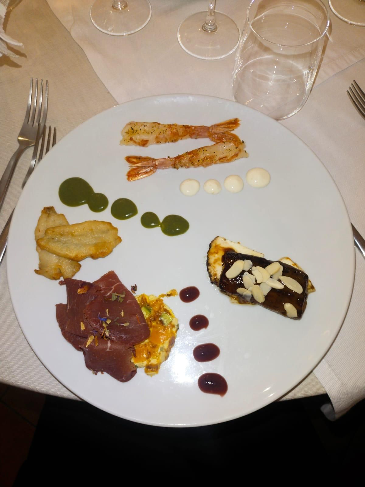 Un piatto bianco con un assortimento di stuzzichini gourmet e qualche filo di salsa su un tavolo di ristorante.
