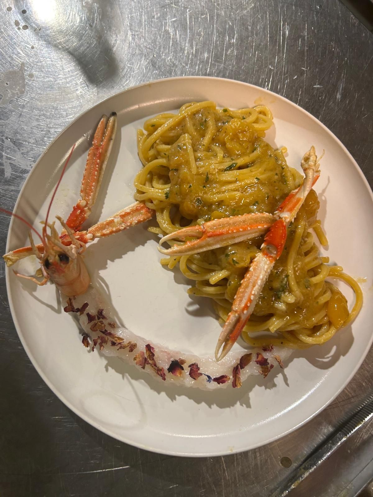 Piatto di pasta con zampe di granchio su un piatto bianco con bordo floreale.
