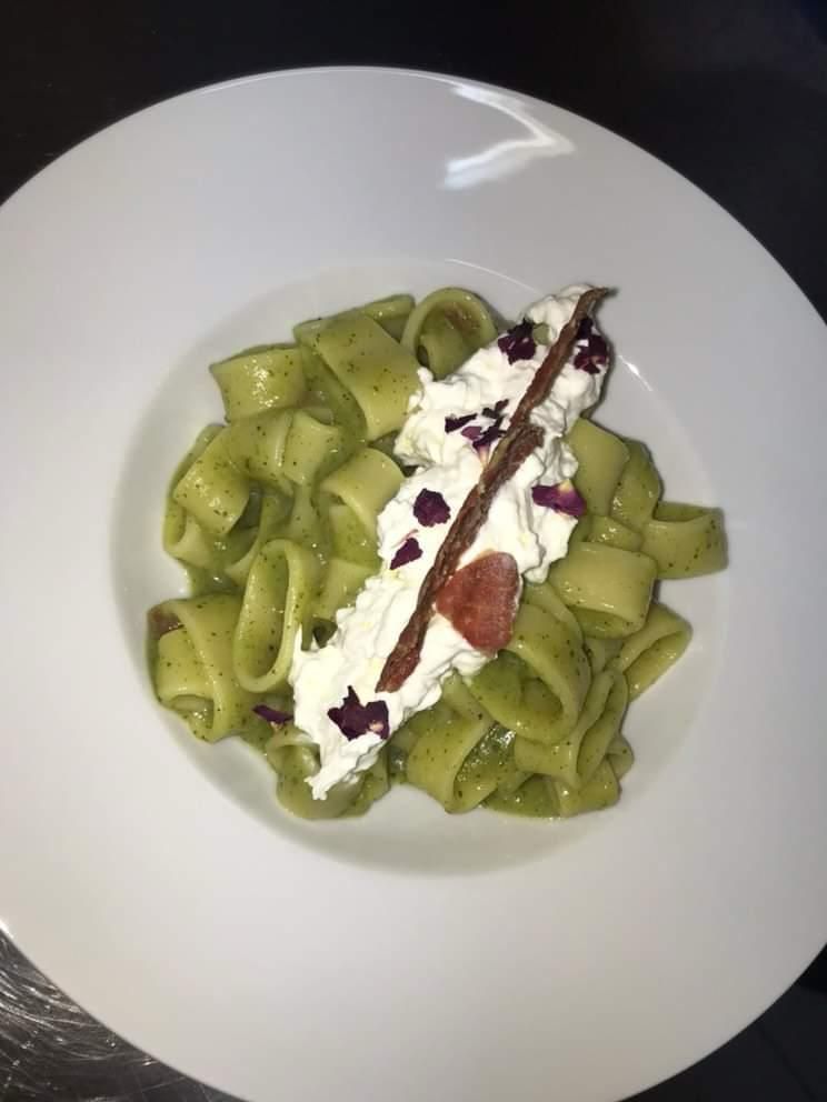 Pasta verde con una cremosa salsa bianca, semi di melograno e una fragola su un piatto bianco.