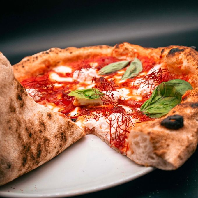 Pizza napoletana su un piatto bianco con salsa di pomodoro, basilico e formaggio fuso.