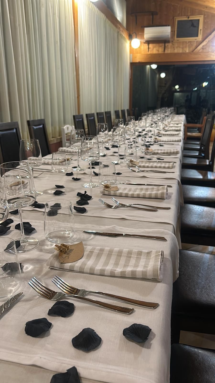 In una sala da pranzo scarsamente illuminata, un lungo tavolo da banchetto apparecchiato con tovaglie bianche, bicchieri e posate.