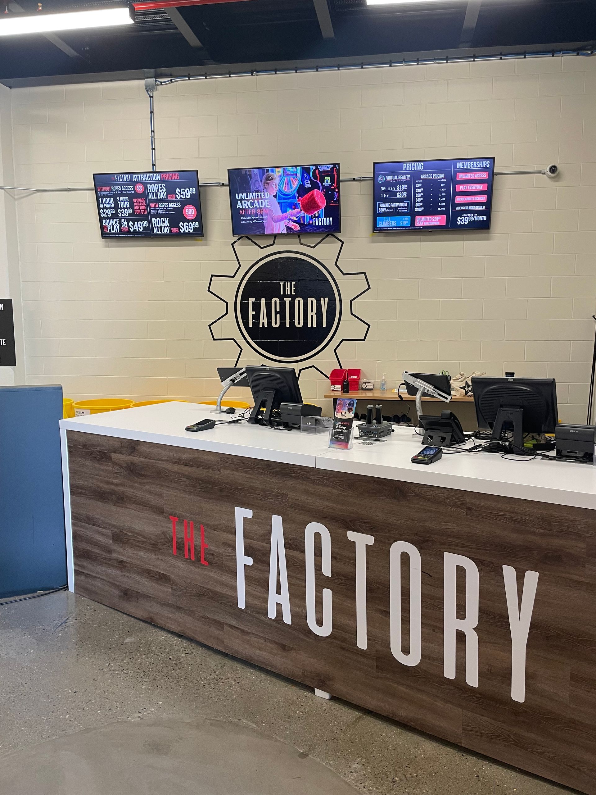 Factory-branded reception counter with three wall monitors and sports memorabilia in a garage-style lobby