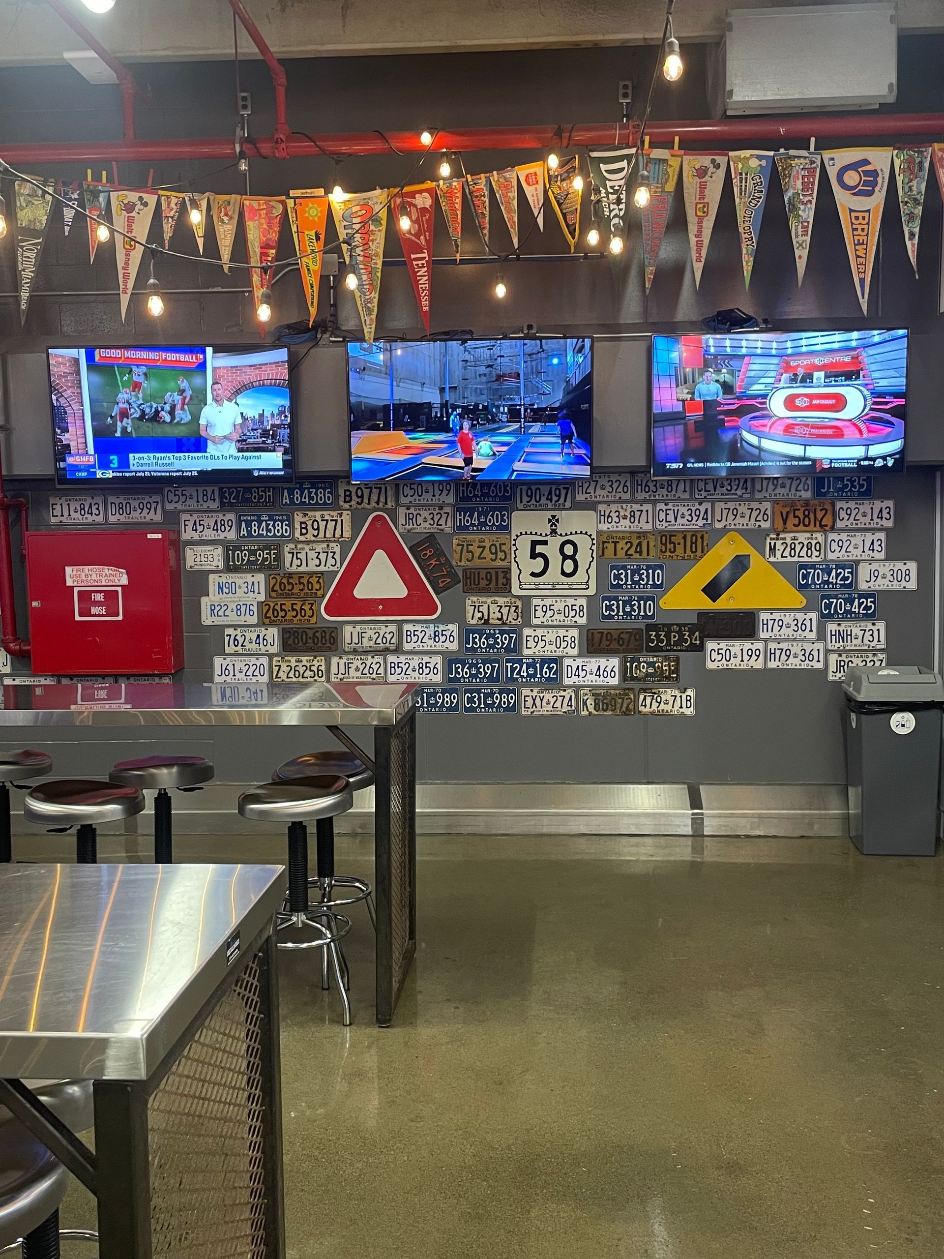 Bar with TVs, hanging decorations, wall signs, and a red donation bin behind empty tables