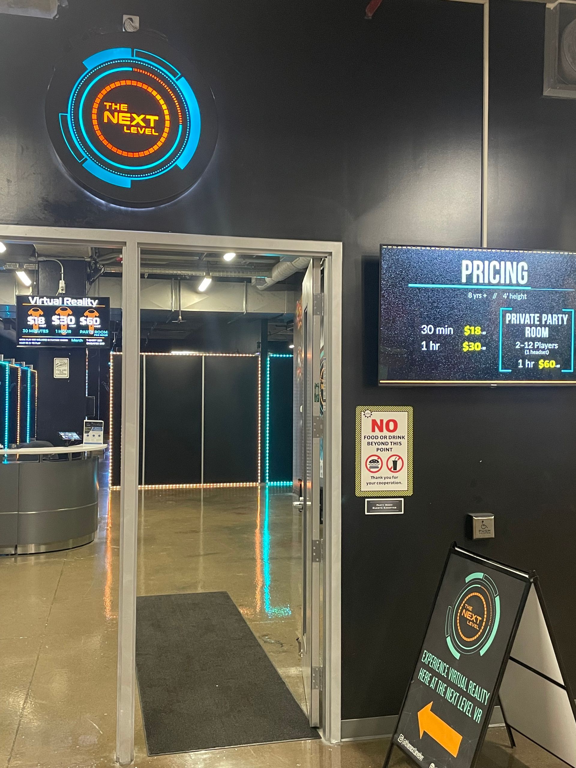 Virtual Reality Games entrance with neon logo, glass doors, and a sign reading “PACHINO” on a dark wall.