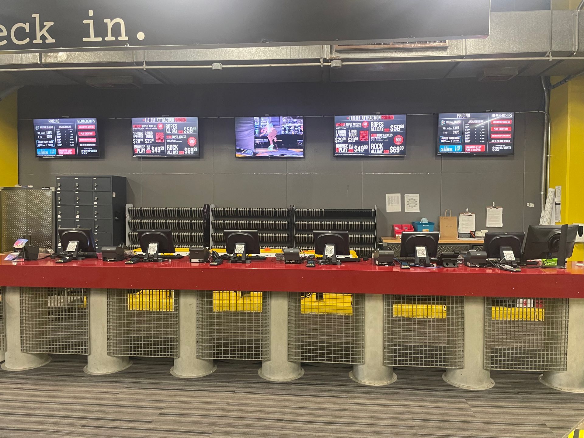 Airport check-in counter with multiple monitors, red counter front, and empty stanchions in front