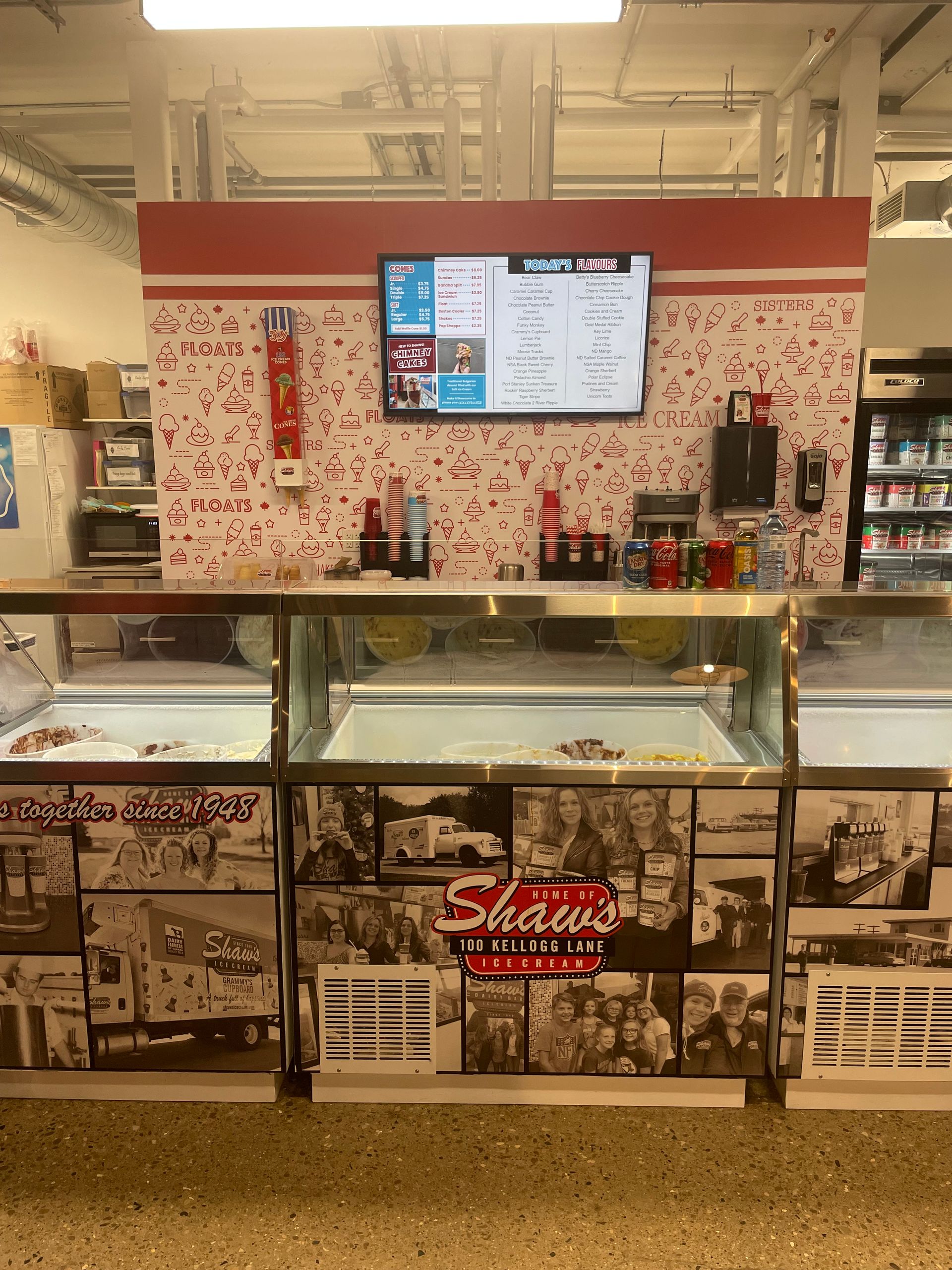 Ice cream prep counter with glass display case, red-and-white walls, and menu screens above.