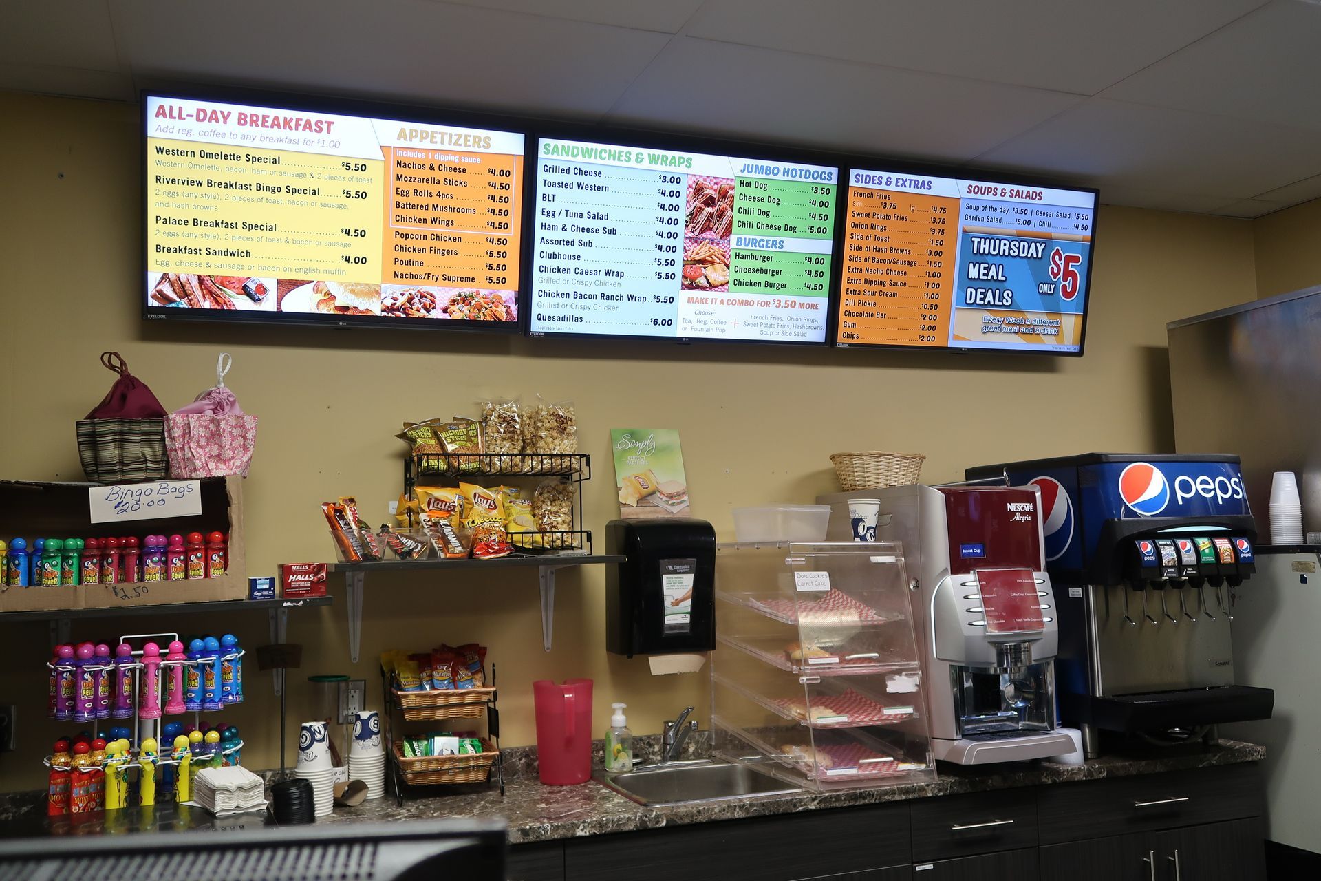 Cafe drink counter with colorful menu boards, snacks, and soda fountain machines