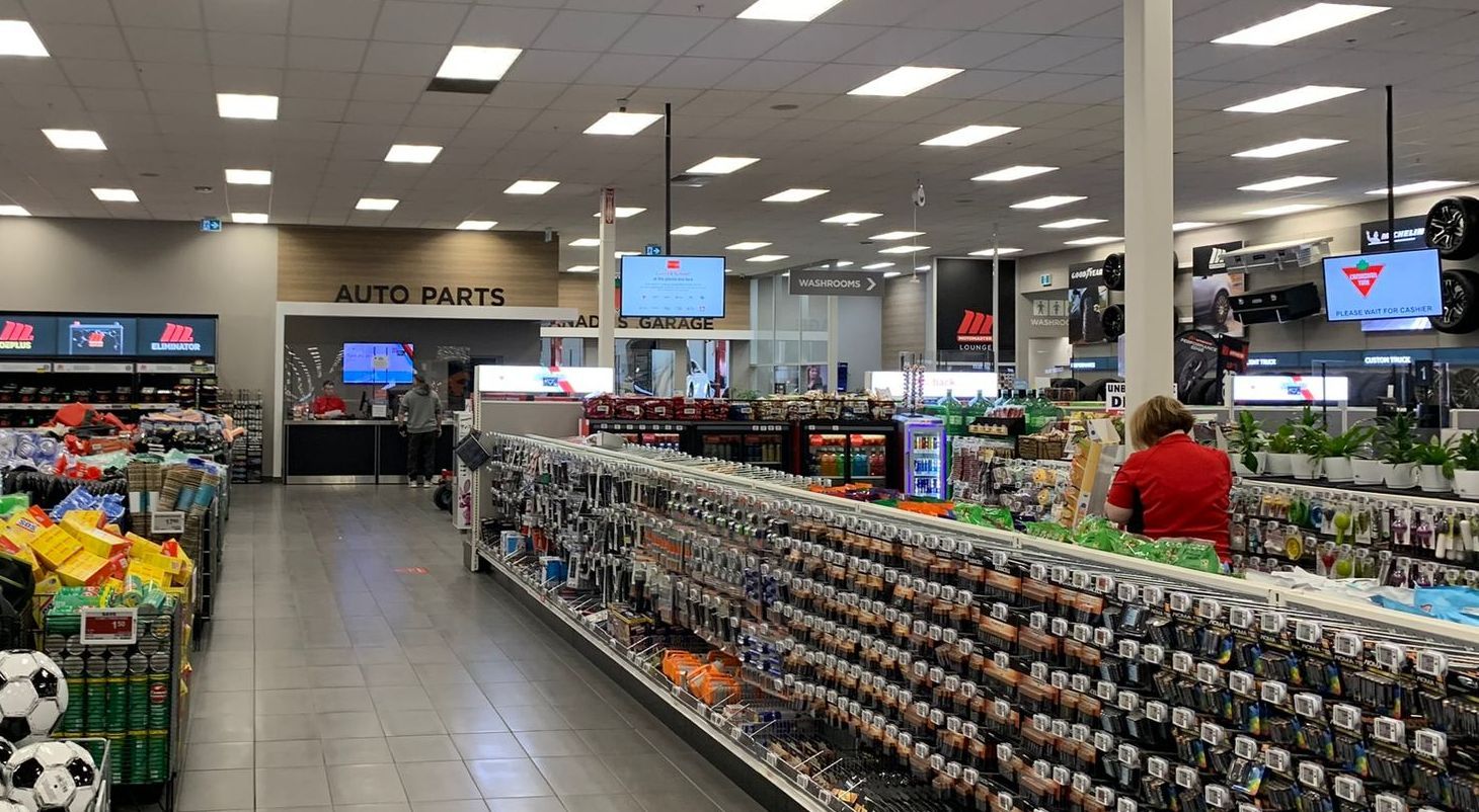 Sports store interior with shelves of merchandise and a person in a red shirt near the aisles and digital signage hanging