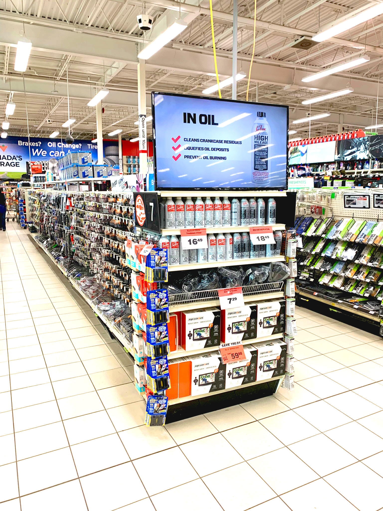Supermarket aisle endcap with hanging TV displaying an in-store ad and shelves of packaged goods underneath