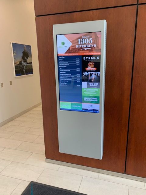 Digital kiosk in a hallway beside a wood-paneled wall, displaying a colorful information screen.