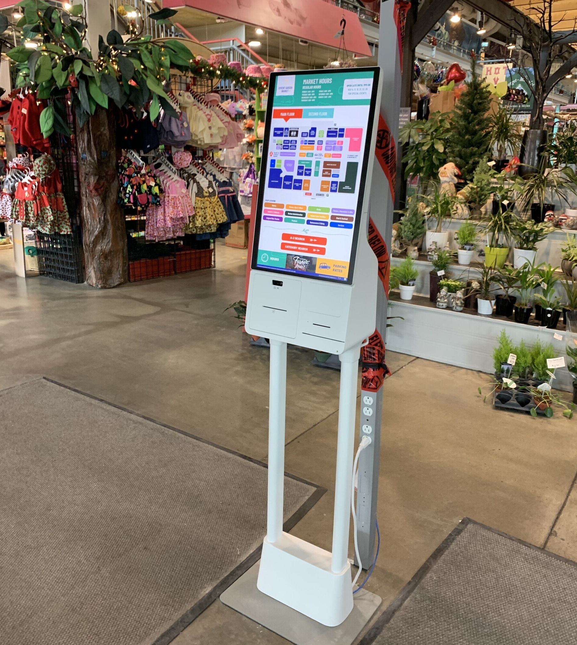 Digital interactive kiosk with colourful screen in a plant-filled store aisle