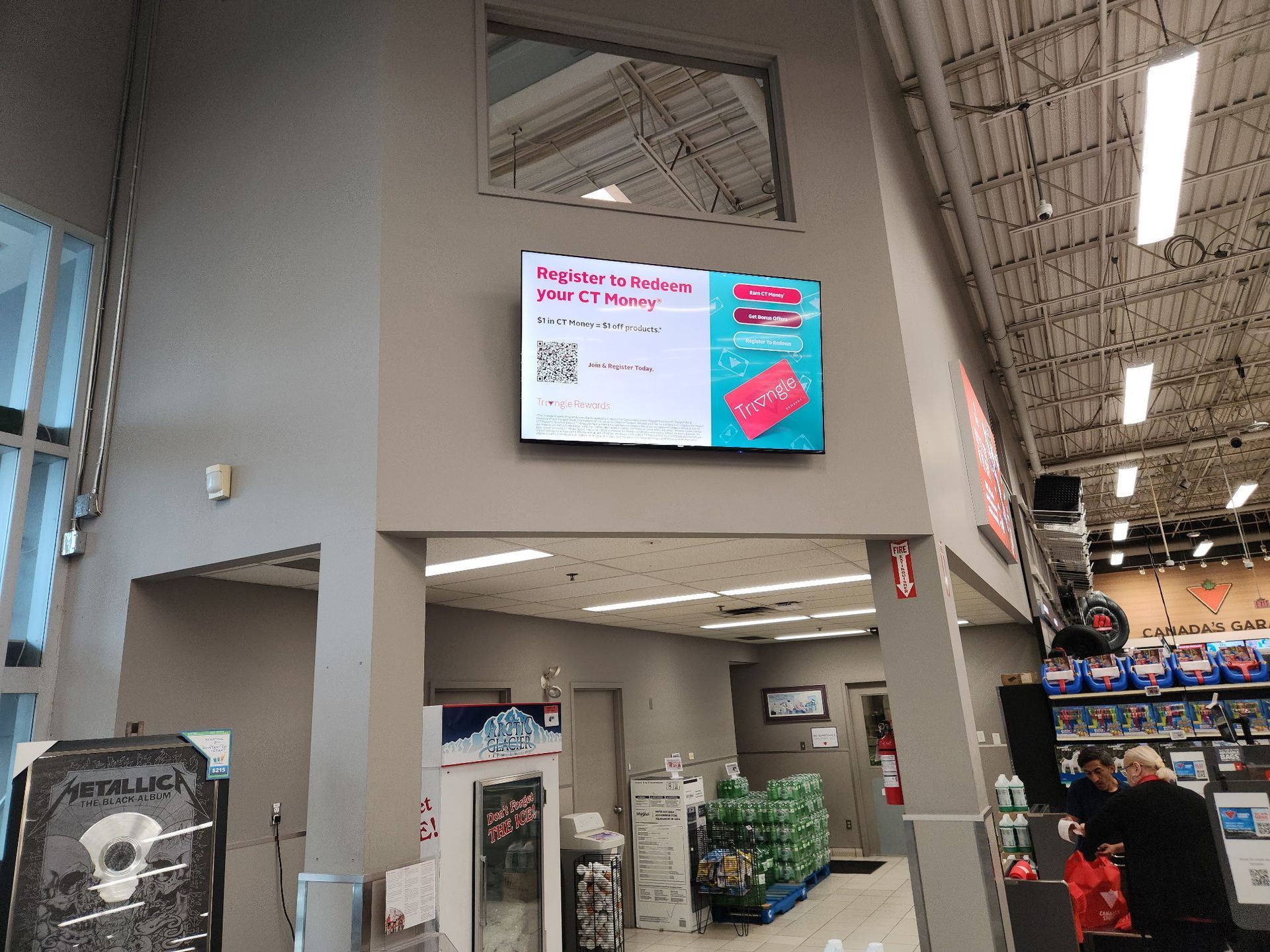 Indoor store aisle with a wall-mounted digital ad screen and shoppers in the background