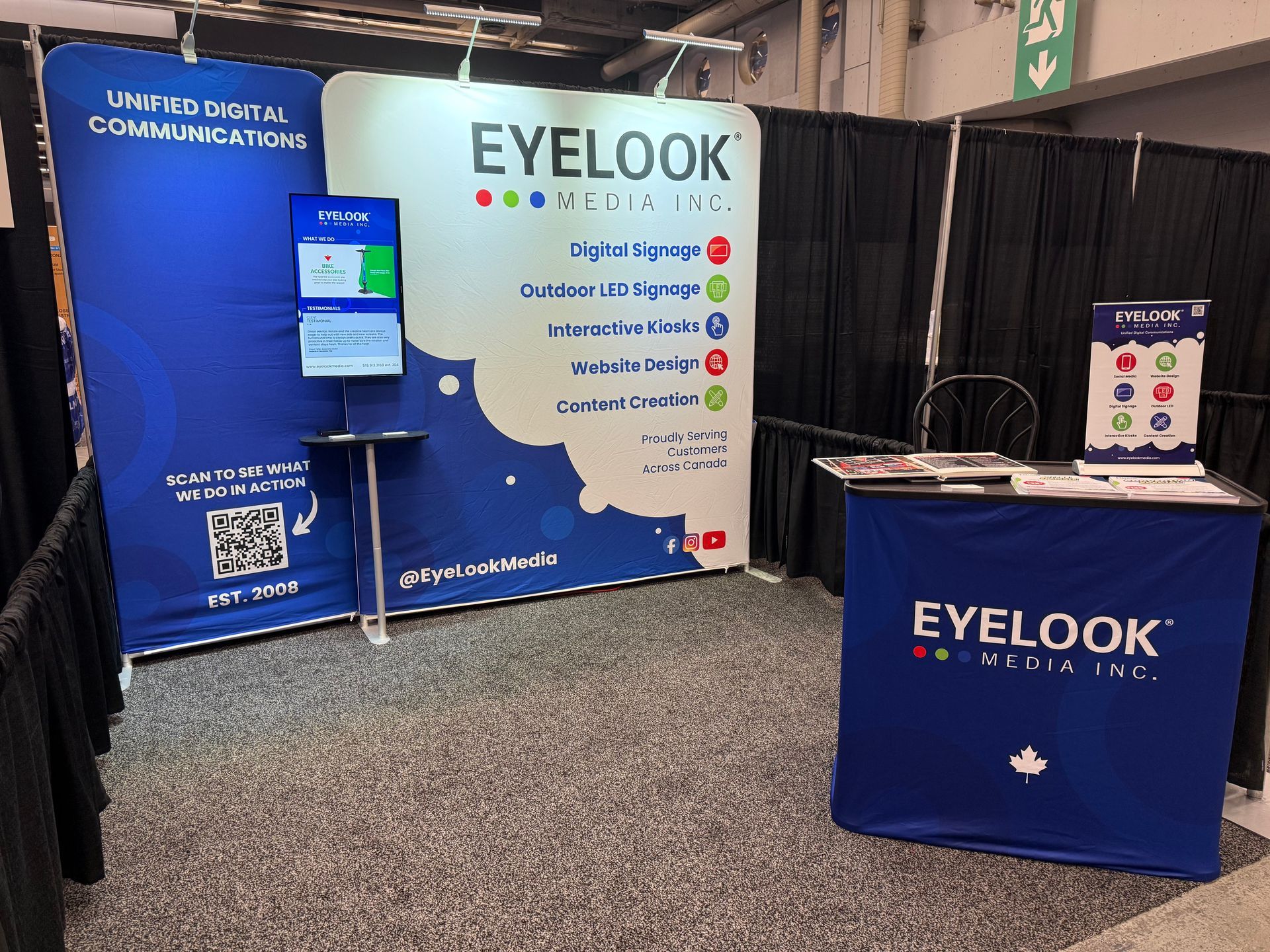 EyeLook Media trade show booth with blue-and-white banners, kiosk screen, and branded table in an exhibition hall