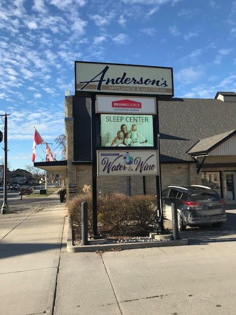 Anderson’s storefront sign on a sunny sidewalk with a parked car and blue sky
