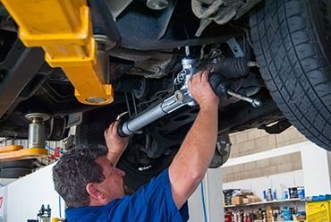 A Man is Working on the Underside of a Car in a Garage — Border Power Steering Service In Lavington, NSW