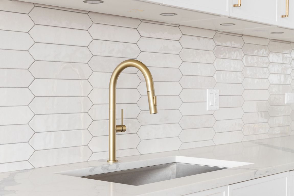 A kitchen sink with a brass faucet and white tiles.