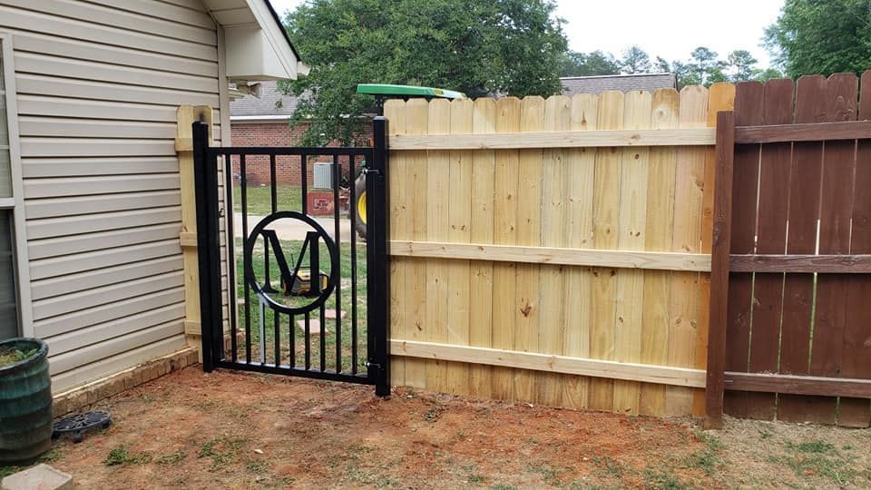 A wooden fence with a metal gate and a monogram on it.