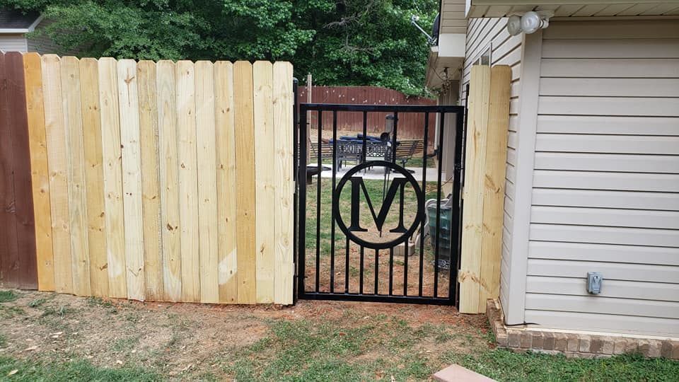 A wooden fence with a metal gate with a monogram on it.