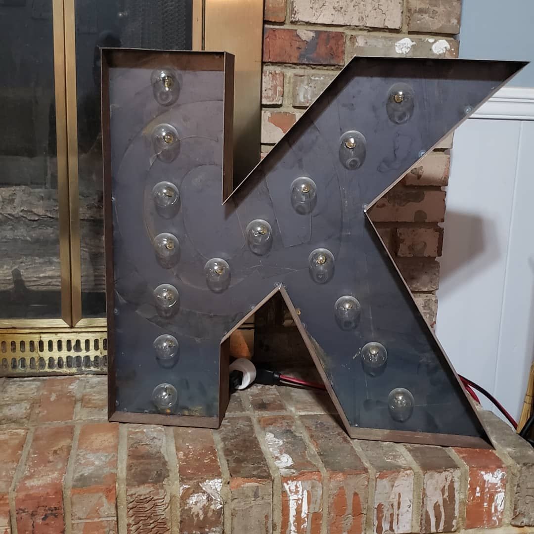 A large metal letter k is sitting on top of a brick fireplace.