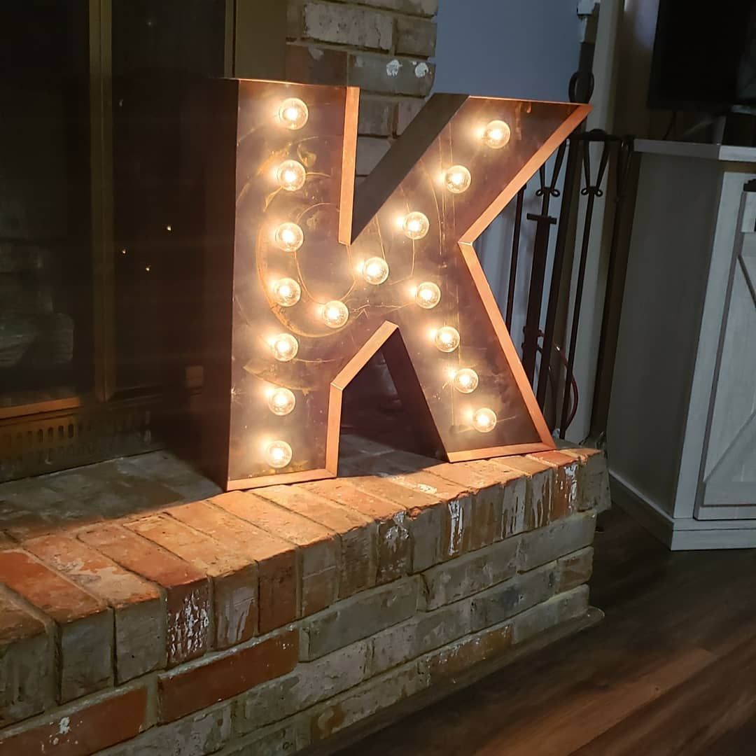 A lighted letter k is sitting on a brick fireplace ledge.