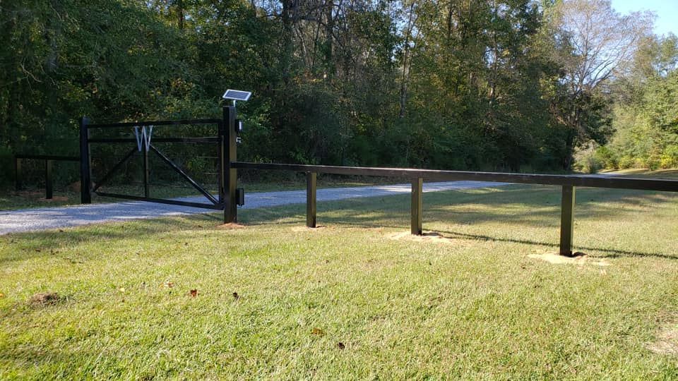 A black gate is sitting in the middle of a grassy field next to a wooden fence.