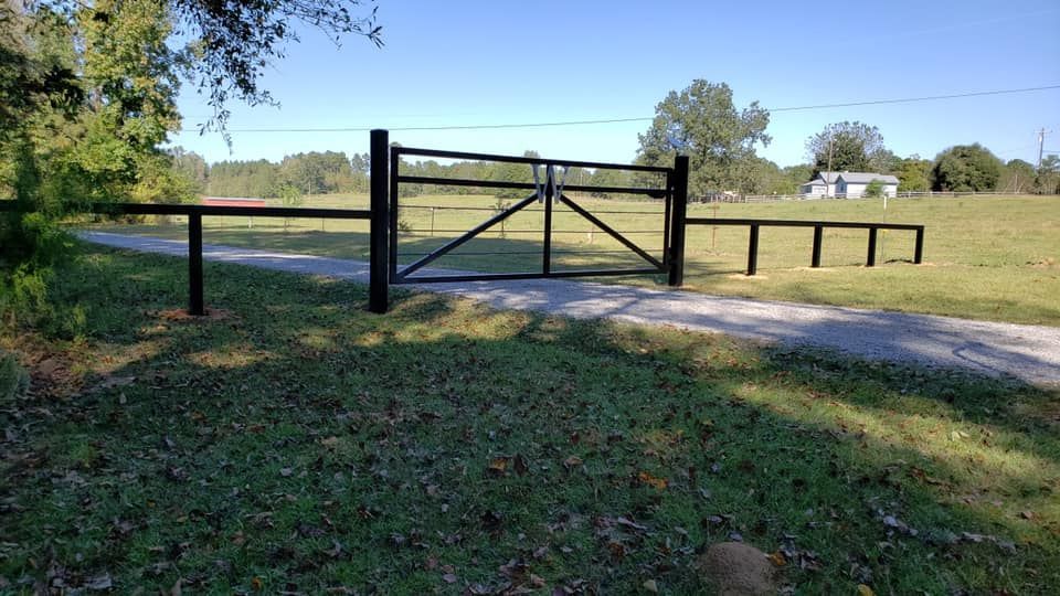 A black gate is sitting in the middle of a grassy field next to a dirt road.