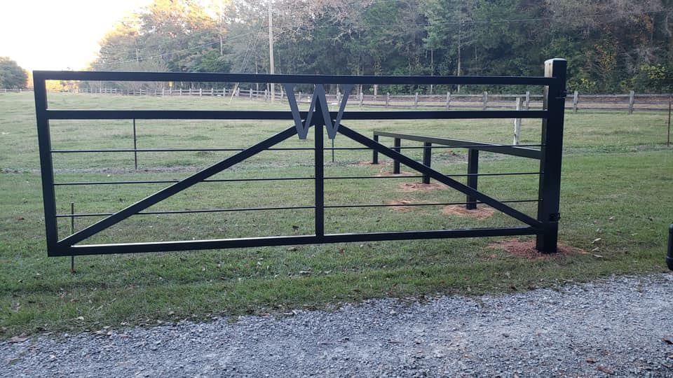 A black metal gate is sitting in the middle of a grassy field.