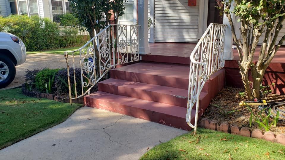 A car is parked in front of a house with stairs and a wrought iron railing.