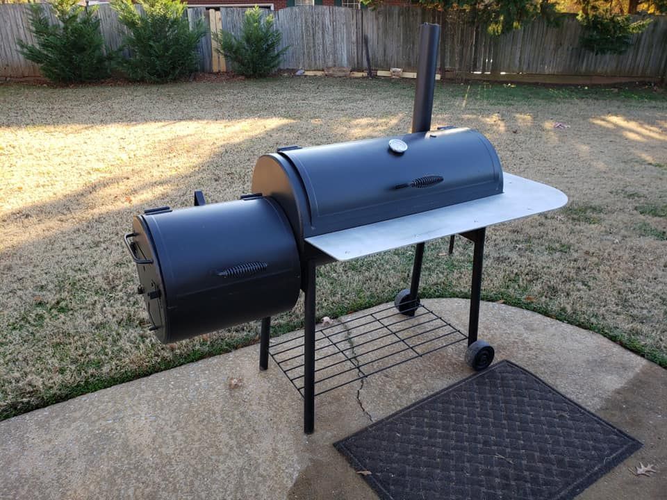 A large black grill is sitting on a concrete patio in a backyard.