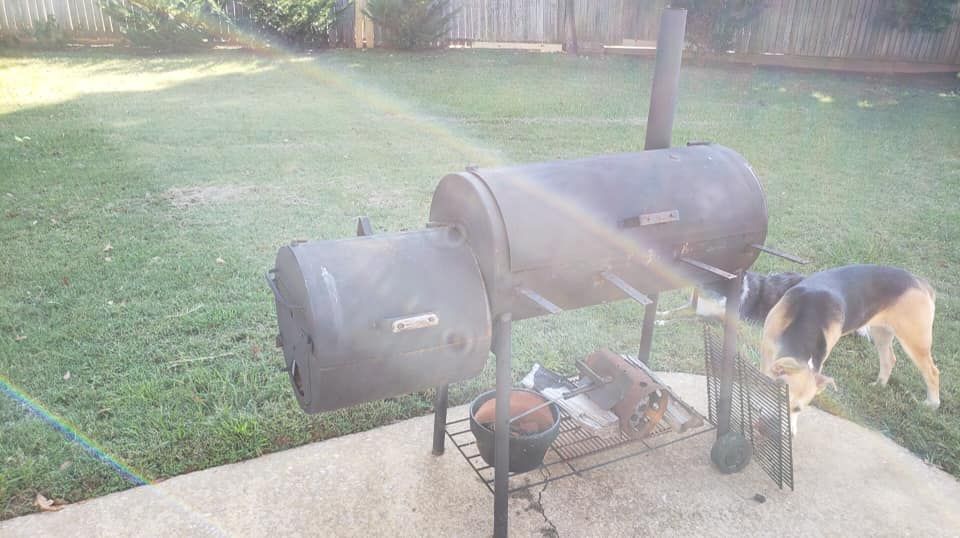 A dog is standing next to a grill in a backyard.