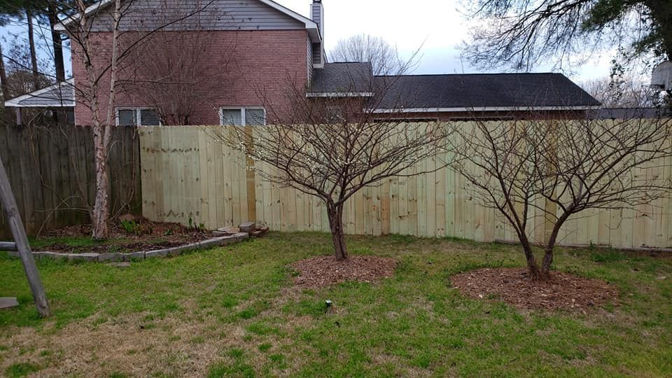 A wooden fence in a backyard with trees and a house in the background.
