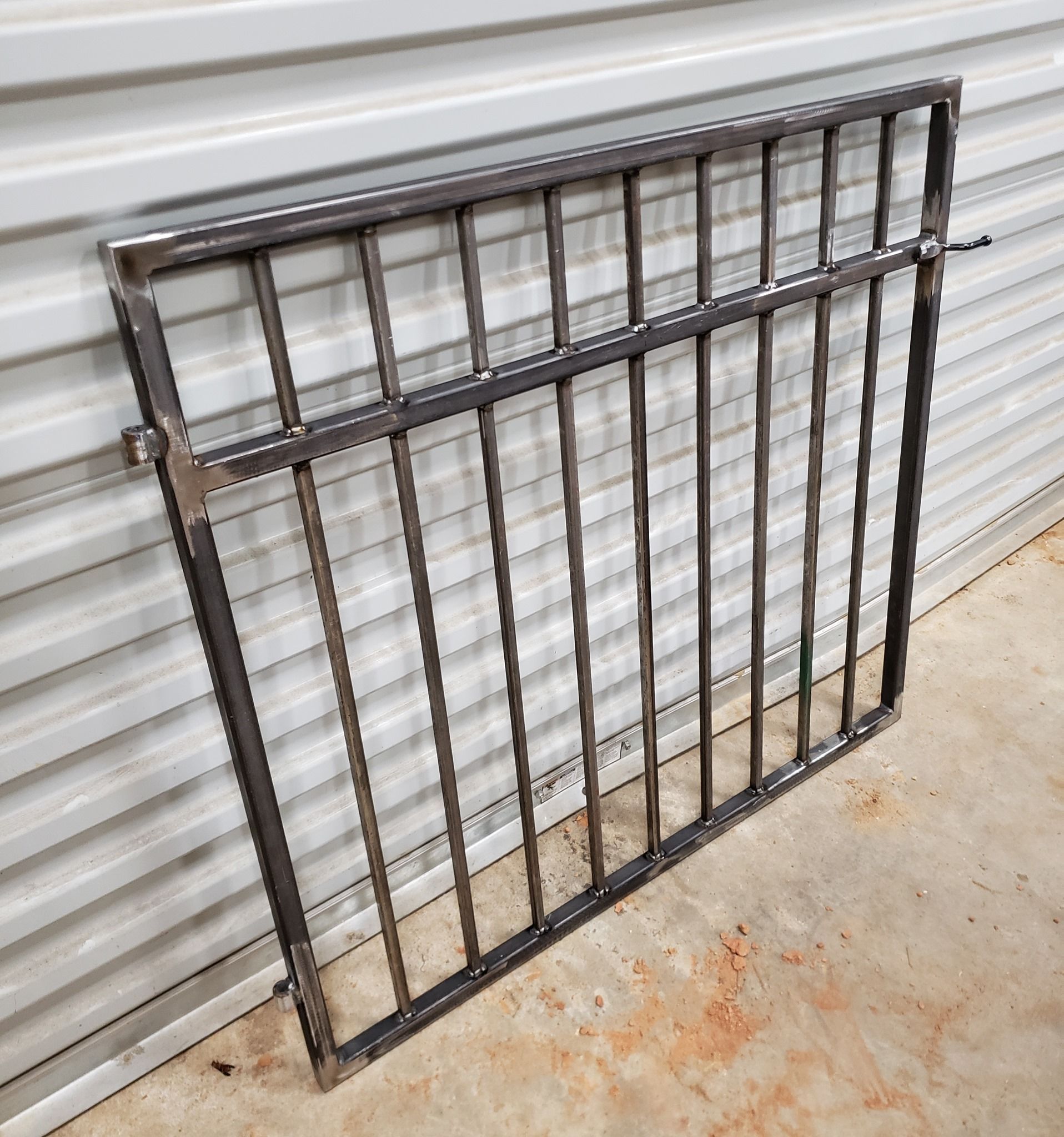 A metal gate is sitting on the ground in front of a white wall.