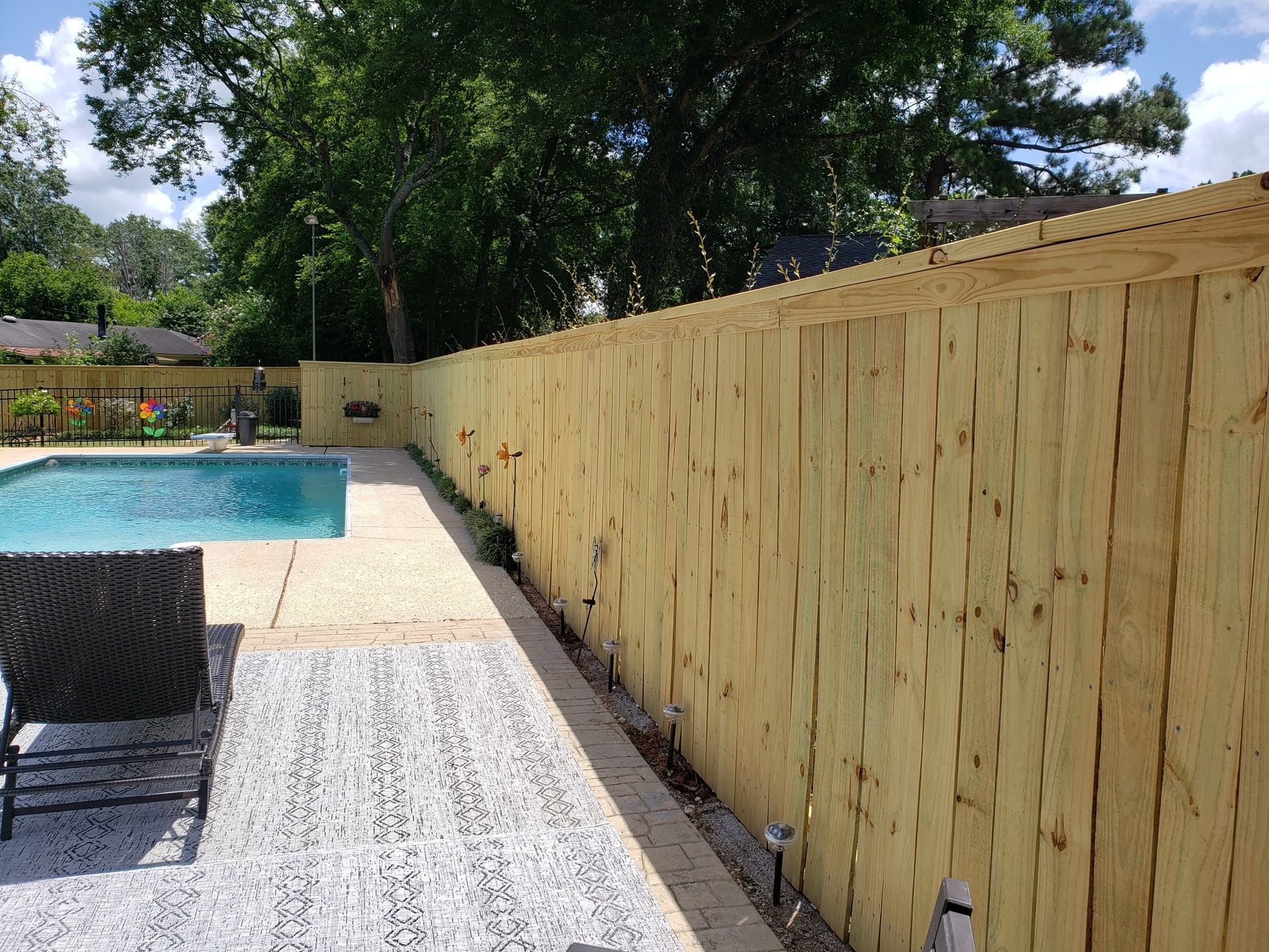 A wooden fence surrounds a swimming pool in a backyard.