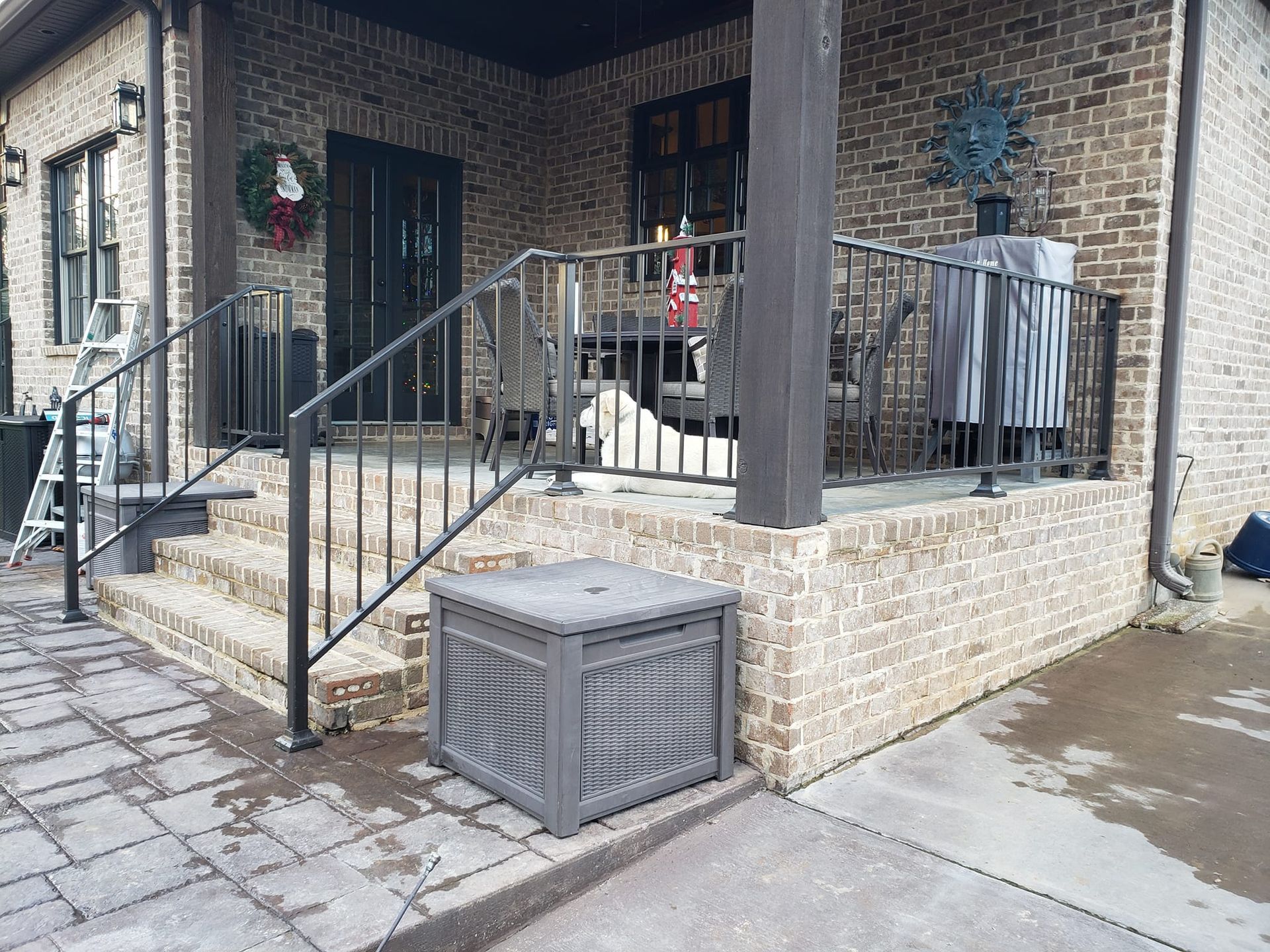 A brick house with a porch and stairs and a box on the sidewalk.
