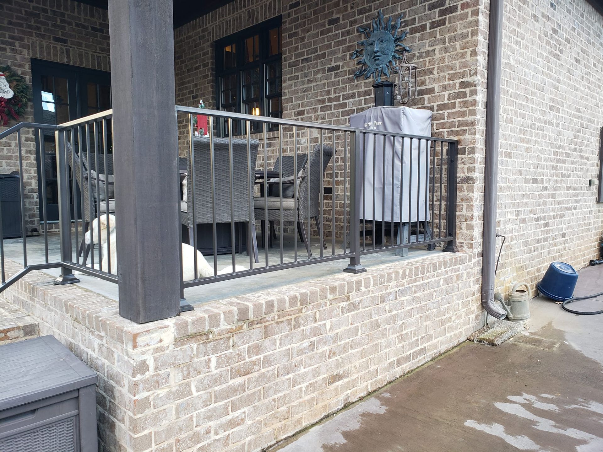 A dog is sitting on a porch next to a brick building.