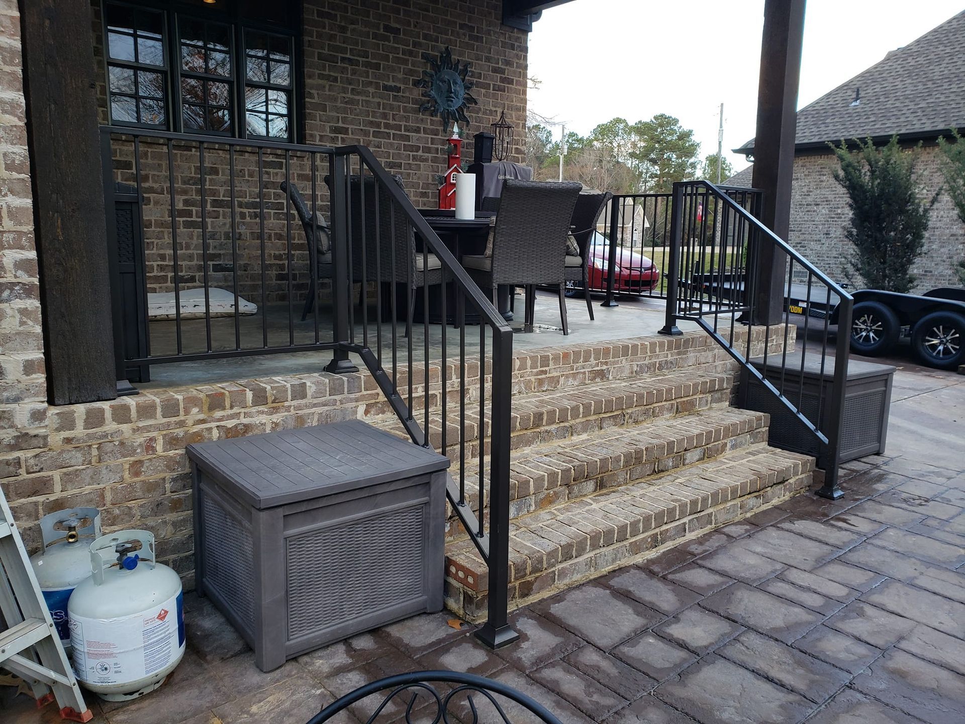 A patio with stairs leading up to a porch with a metal railing.
