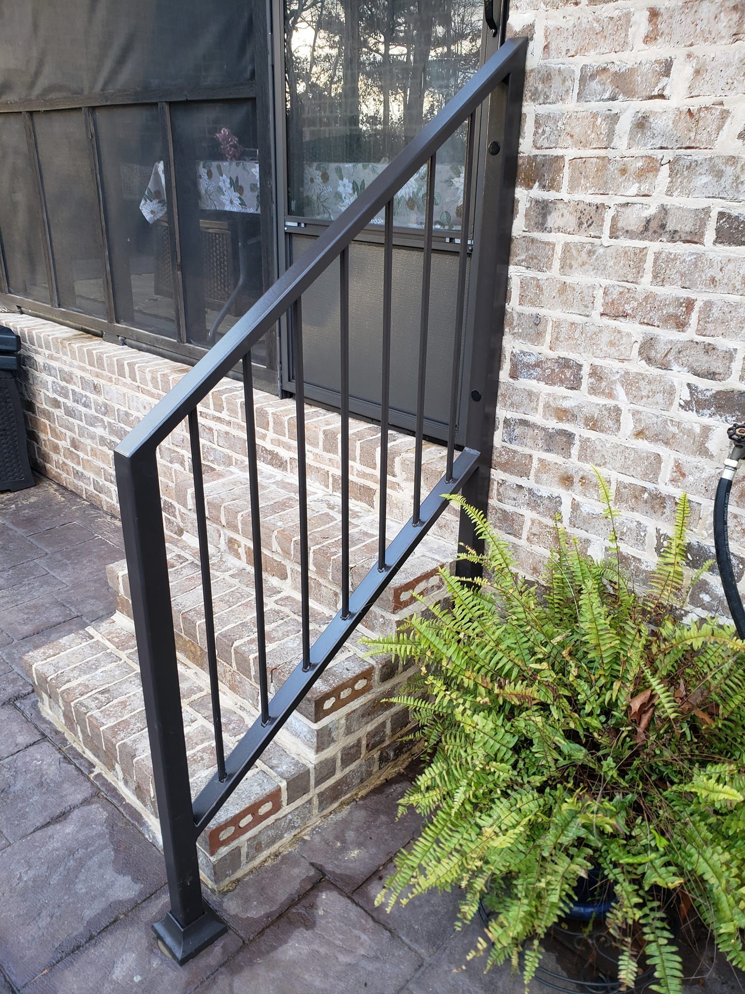 A black railing is sitting on the side of a brick building next to a potted plant.