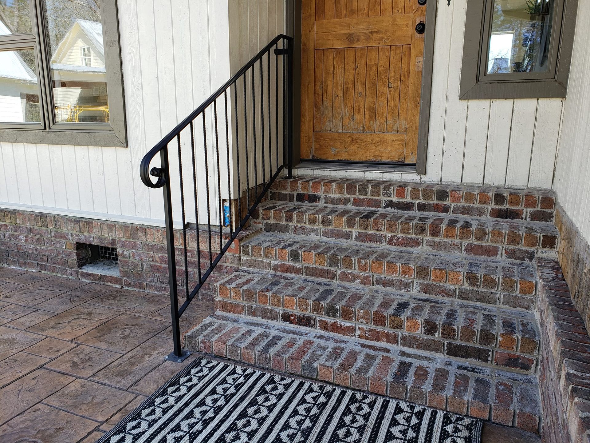 A brick porch with a wrought iron railing and a rug.
