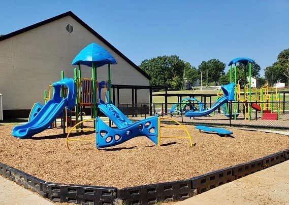 A playground with a slide and swings in front of a building