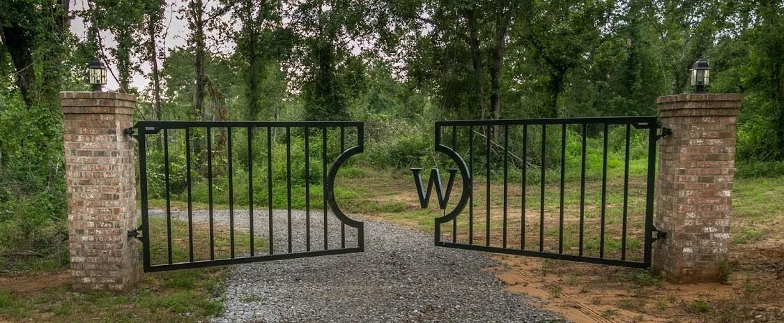 A gate with the letter w on it is open to a dirt road.