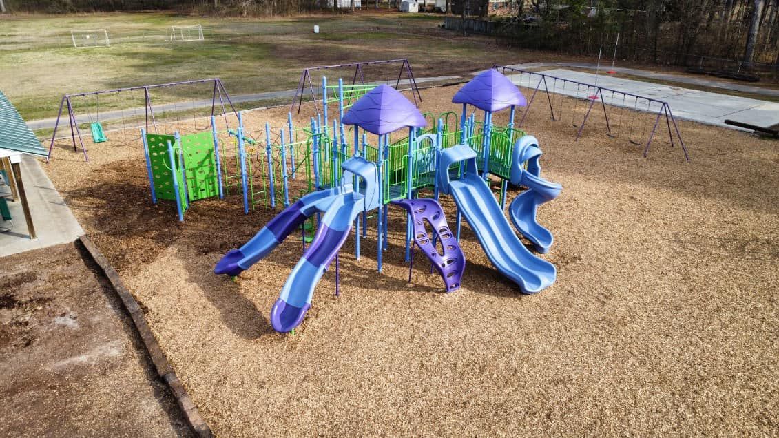 An aerial view of a playground with purple and blue slides and umbrellas.