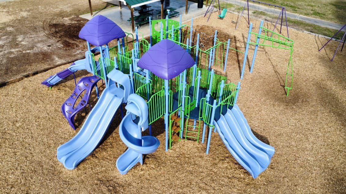 An aerial view of a playground with blue slides and purple umbrellas.