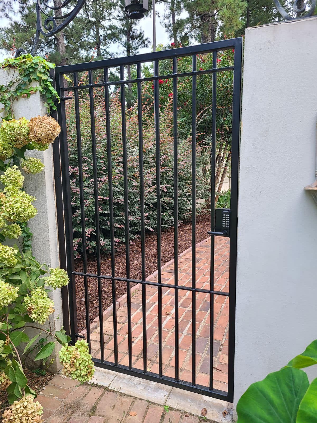 A black wrought iron gate is open to a brick walkway.