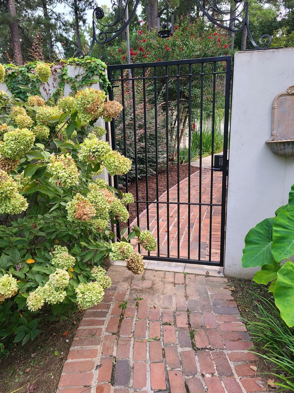 A brick walkway leading to a gate surrounded by flowers and bushes.