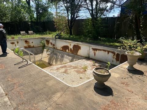 A man is standing next to a rusty swimming pool in a backyard.