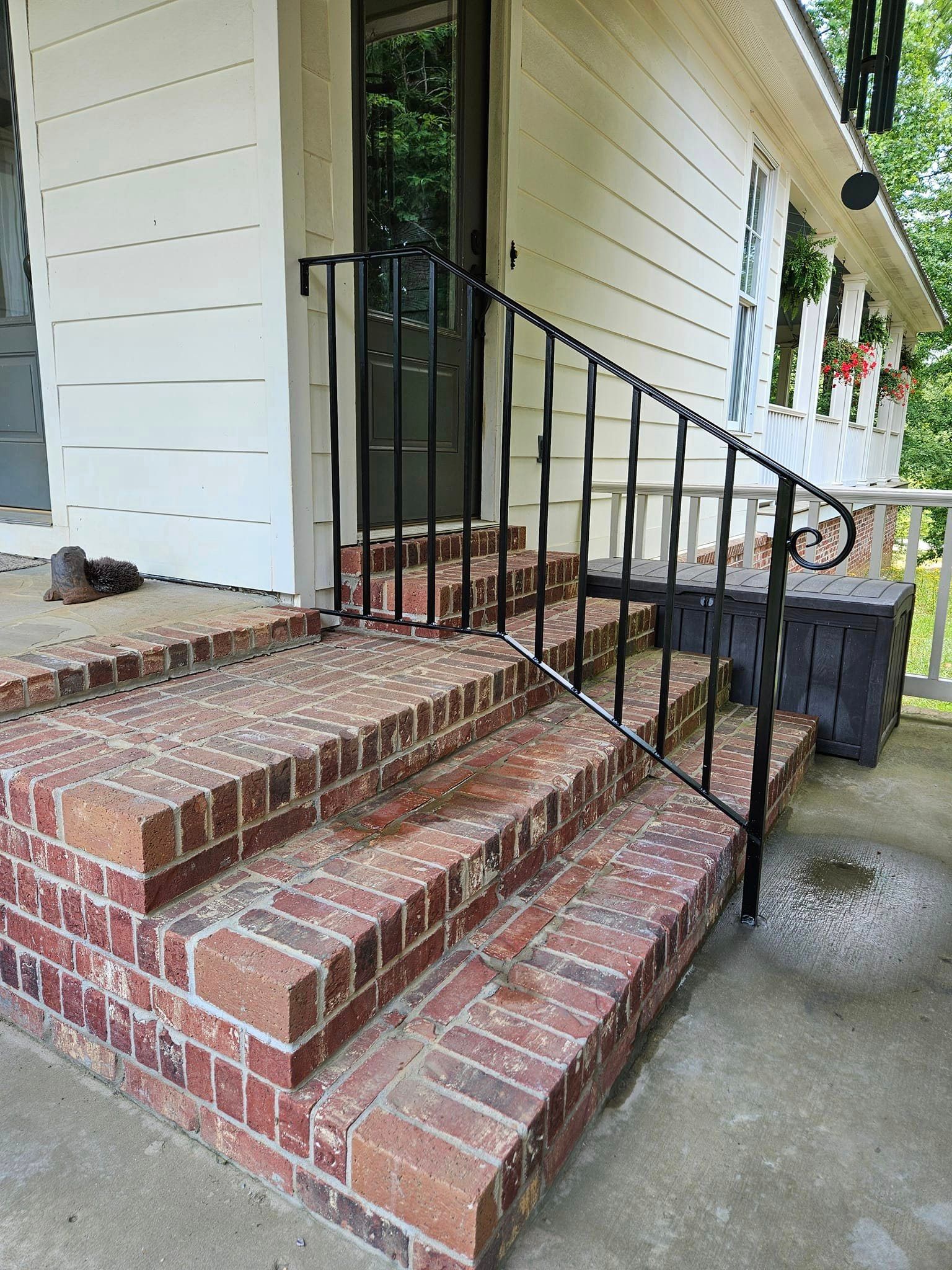 A white house with brick steps and a black railing on the porch.