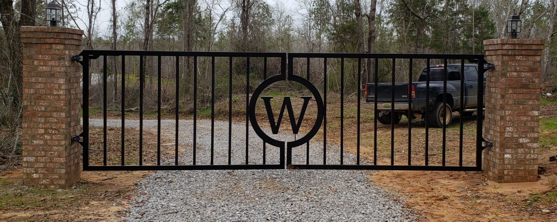 A black gate with the letter w on it and a car parked behind it.