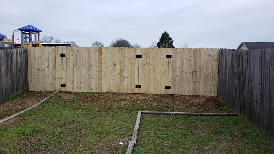 A wooden fence in a backyard with a playground in the background.