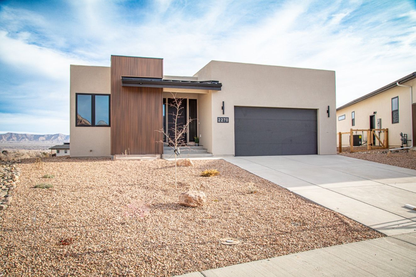 Tan stucco house with gray garage door, gravel yard, and blue sky.