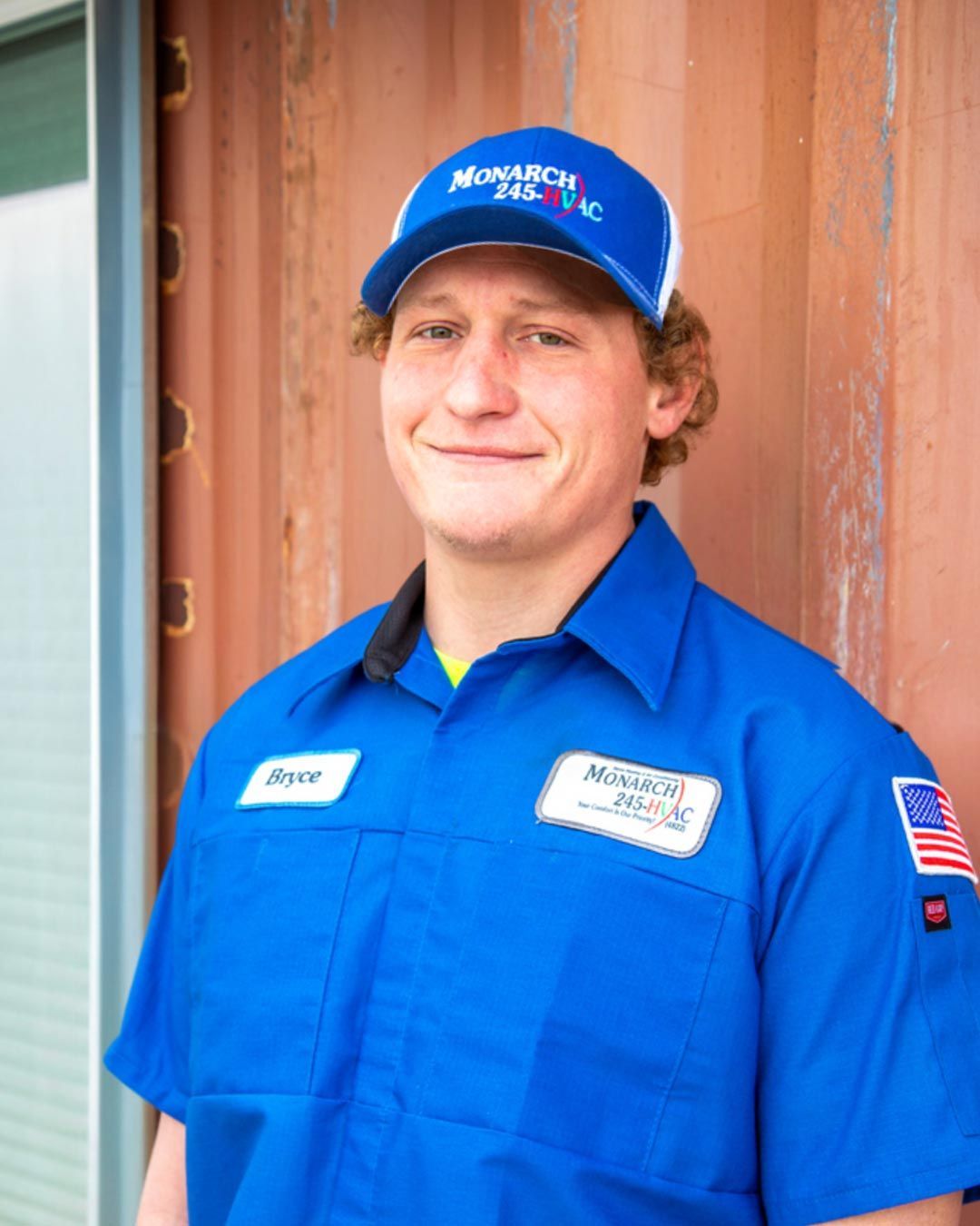 Man wearing a blue uniform and cap with the company logo. He's smiling, standing near a brown storage container.